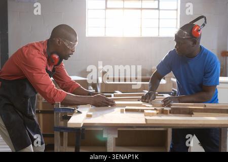 Deux charpentiers alignent et mesurent des planches de bois sur un établi en bois à l'intérieur de l'atelier de menuiserie Banque D'Images