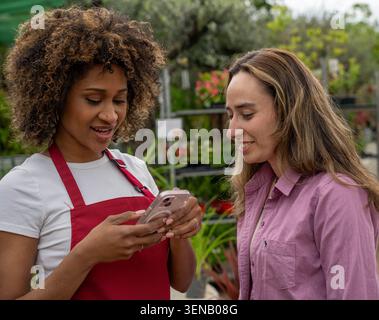 Deux femmes vérifiant un smartphone dans un centre de jardinage Banque D'Images