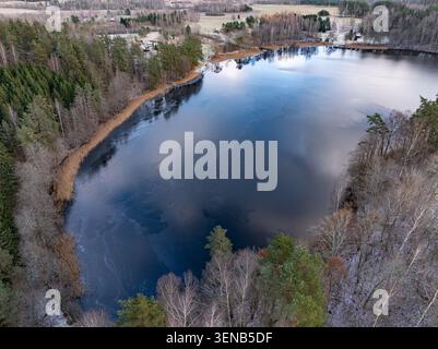 Vue aérienne du lac Dubuļkas avec de la glace mince et le littoral boisé en hiver, Latgale, Lettonie Banque D'Images