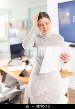 Triste jeune femme avec document au bureau Banque D'Images