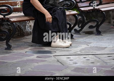 Femme en robe noire et baskets blanches assise et au repos, vue en angle élevé Banque D'Images