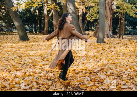 Femme marche à travers le parc rempli de feuilles d'automne tombées tout en regardant en arrière. Vacances à faible empreinte carbone, industrie des loisirs en plein air d'automne Banque D'Images