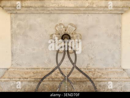 Fontaine murale en pierre historique avec bec décoratif et support en fer forgé Banque D'Images