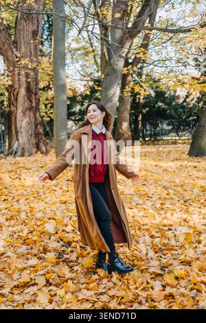 Femme marche à travers le parc rempli de feuilles d'automne tombées tout en regardant en arrière. Vacances à faible empreinte carbone, industrie des loisirs en plein air d'automne Banque D'Images