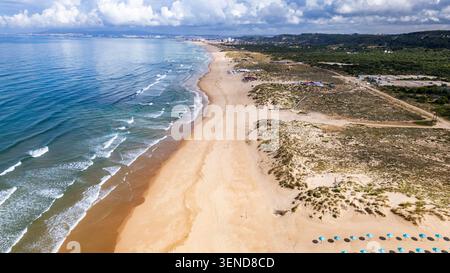 Costa Caparica, Lisbonne. Vue aérienne de la plage Costa Caparica. Le sable doré rencontre les vagues bleues de la mer. Des parapluies turquoises parsèment le rivage. Dunes et verdure l Banque D'Images