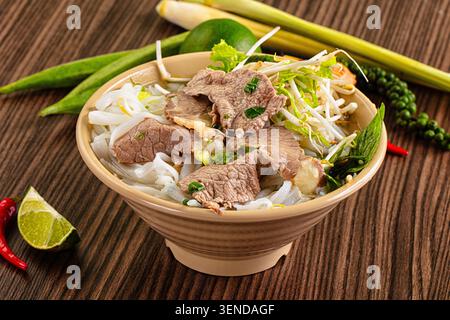 Bol appétissant de soupe traditionnelle vietnamienne de nouilles de bœuf pho, garni d'herbes fraîches, de germes de haricots, de citron vert tranché sur une table en bois rustique Banque D'Images