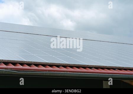Perspective à faible angle de panneaux solaires sombres installés sur le toit d'une maison résidentielle contre un beau ciel nuageux. Démontre un développement durable moderne Banque D'Images