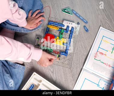 Kit de circuit électronique d'assemblage enfant génération Alpha sur plancher gris. mains de fille insérant les piles dans le bloc en plastique en suivant le schéma Banque D'Images