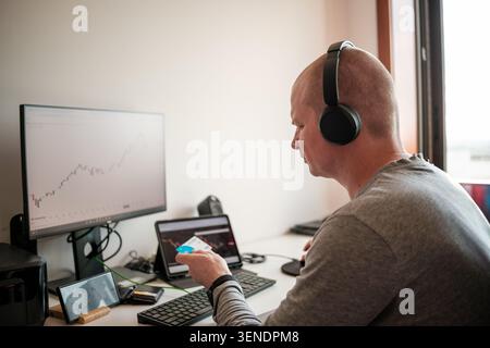 Homme portant des écouteurs surveillant les graphiques financiers sur plusieurs écrans Banque D'Images