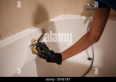 Main avec un gant noir frottant une poignée de baignoire à l'aide d'une éponge Banque D'Images