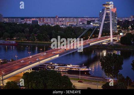 Illuminé la plupart des ponts SNP enjambant le Danube la nuit avec un grand bateau de croisière de passagers sous la structure, Bratislava, Slovaquie, Euro Banque D'Images