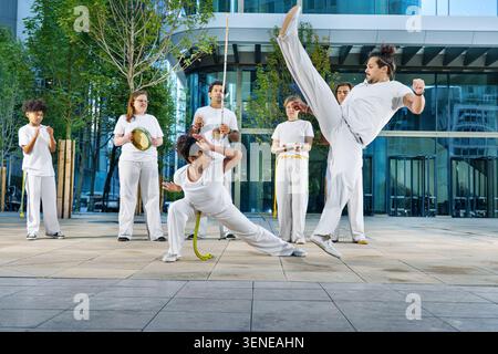 Un groupe de sportifs d'âges différents s'entraînant à la capoeira dans une grande ville Banque D'Images