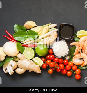Set spécial pour une soupe épicée thaïlandaise authentique Tom-yum kung. Citron vert, galanga, piment rouge, tomate cerise, citronnelle et feuille de citron vert kaffir sur table noire avec espace de copie sur tableau noir. Vue de dessus. Image carrée. Banque D'Images