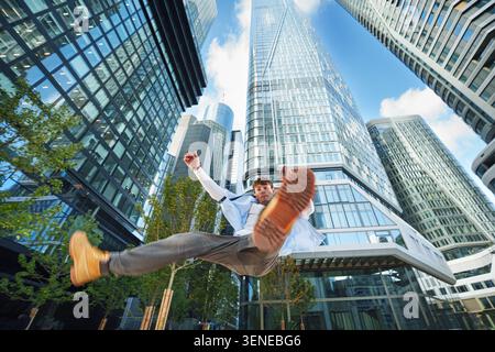 Jeune homme saute dans la ville urbaine et moderne en plein air, équilibrant en milieu d'air isolé sur fond de ciel bleu. Banque D'Images