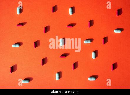 Des capsules assorties de couleurs blanches et roses sont disposées sur un fond orange, affichant différentes formes et tailles de médicaments dans une vie plate Banque D'Images