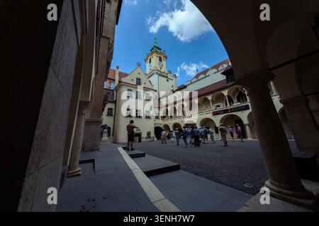 Un groupe de touristes explorant une cour européenne historique avec une architecture ancienne, des arcades et une tour de l'horloge sous un ciel bleu. Banque D'Images