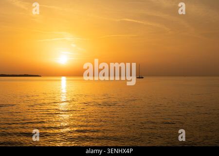 Coucher de soleil doré sur la mer calme avec silhouette de voilier près de l'horizon Banque D'Images