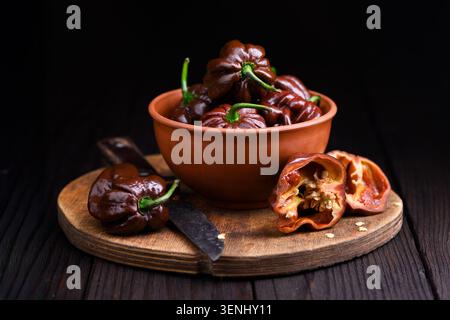 Poivrons habanero au chocolat avec des morceaux coupés dans un bol sur fond sombre. Gousses de Chili frais composition rustique texture naturelle Banque D'Images