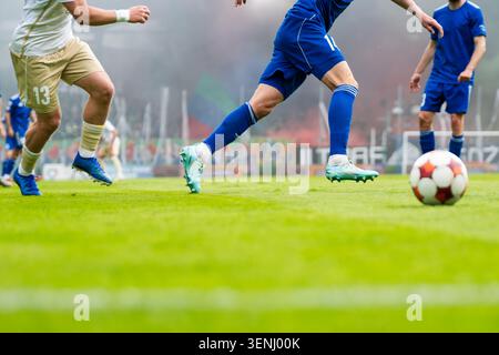 Gros plan de joueurs de football en uniformes bleus et blancs courant vers le ballon sur le terrain vert, scène de sport d'action réelle. Banque D'Images