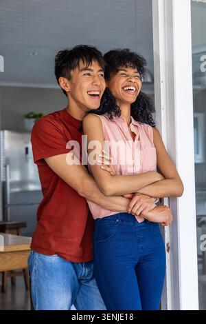 Vidéo verticale : partenaire enveloppant les bras, couple riant à la porte de la cuisine près du réfrigérateur en rouge et rose Banque D'Images