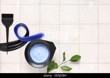 Outils de teinture des cheveux avec des brins de cheveux bleus et noirs, bol de mélange et brosse sur fond carrelé blanc Banque D'Images