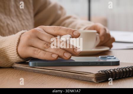 Femme main tenant le stylo stylet sur smartphone et ordinateur portable avec tasse à café sur la table en bois, une tasse à café blanche se trouve sur une soucoupe en arrière-plan, un Banque D'Images