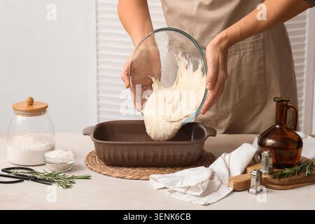 Femme versant la pâte fraîchement préparée du bol en verre dans le plat de cuisson pour le pain ou la pâtisserie maison, divers ingrédients de cuisson et outils sont disposés Banque D'Images