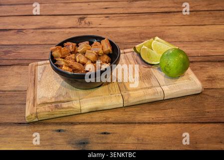 Ventre de porc rillons brésilien traditionnel servi avec des quartiers de citron vert sur bois. Un éclairage chaleureux accentue les textures riches et invitantes des aliments. Parfait conce alimentaire Banque D'Images
