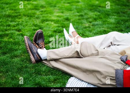 Couple afro-américain à la mode allongé sur la pelouse verte dans le parc de détente profitant de la journée à l'extérieur. Banque D'Images