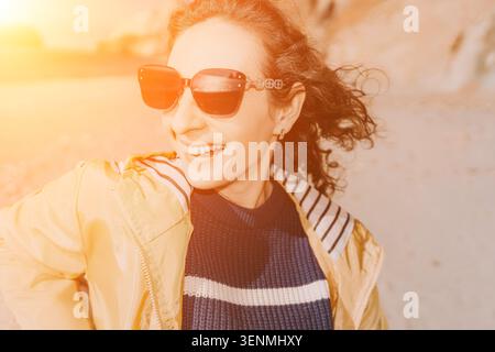 Femme lunettes de soleil plage heureuse voyageuse féminine en veste jaune appréciant la lumière chaude du coucher de soleil à l'espace de copie de bord de mer Banque D'Images