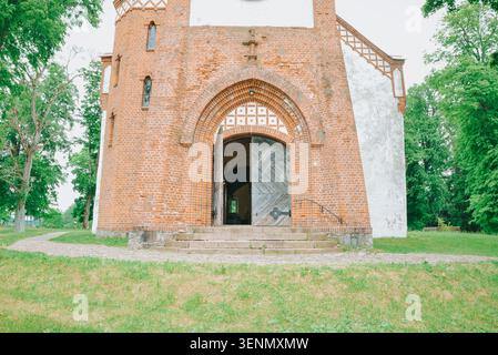 Riga, Lettonie - 5 juin 2026 : vue de face d'une église historique en briques avec une entrée voûtée et une porte en bois ouverte, entourée d'une végétation luxuriante. Idée Banque D'Images
