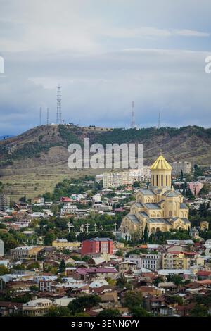 Une vue panoramique imprenable capture la grandeur de la cathédrale Holy Trinity Sameba avec son dôme doré niché dans le paysage urbain tentaculaire de Banque D'Images