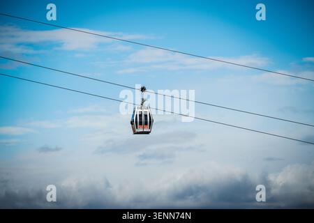 Une cabine de téléphérique moderne solitaire, blanche et grise avec des accents intérieurs rouges subtils, glisse dans le ciel soutenu par de solides câbles aériens. Le ca Banque D'Images
