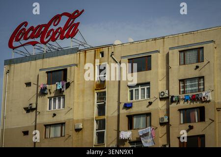 Un grand panneau rouge Coca-Cola se trouve bien en vue au sommet d'un immeuble d'appartements de plusieurs étages altéré avec de nombreuses fenêtres et des unités de climatisation. Vêtements Banque D'Images