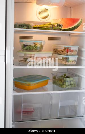 Réfrigérateur ouvert rempli de récipients de préparation de repas sains, légumes frais, fruits et plats préparés. Banque D'Images