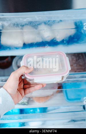 vue de dessus d'un homme tenant un récipient scellé rempli d'aliments surgelés juste pris du tiroir du congélateur, avec du givre recouvrant le plastique et réfrigéré Banque D'Images