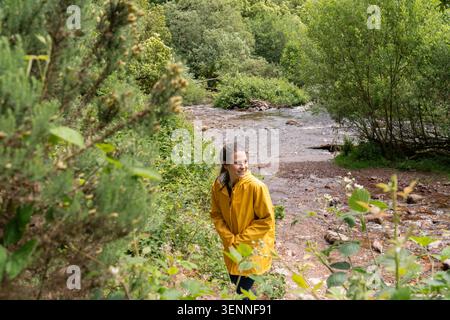 Femme portant un imperméable jaune explorant la nature par la rivière Banque D'Images
