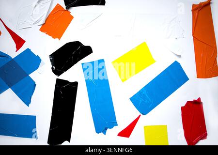 Des morceaux de film plastique déchiré de plusieurs couleurs sont dispersés sur une surface blanche, affichant une variété de formes et de textures dans un arran visuellement frappant Banque D'Images