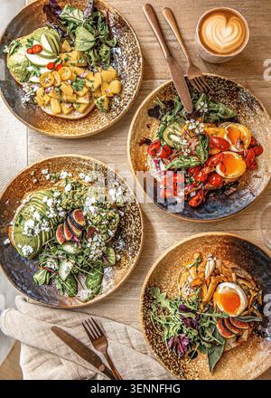 Une vue de haut en bas d'une table en bois avec quatre assiettes de plats de petit déjeuner colorés et une tasse de café Latte art. Banque D'Images