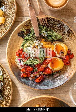 Pain grillé artisanal au levain garni d'une salade de tomates vibrante, de basilic frais et d'œufs durs coupés en deux, servi sur une assiette rustique en céramique. Banque D'Images