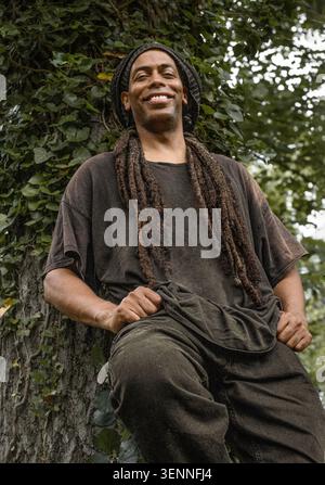 Homme heureux avec des dreadlocks se relaxant contre un lierre Banque D'Images