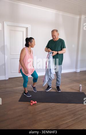 Couple asiatique exerçant à la maison, homme tenant un sweat-shirt, femme senior soulevant le genou sur un tapis noir Banque D'Images