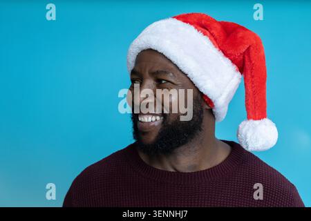 Homme afro-américain adulte souriant, portant chapeau de Père Noël et pull Bordeaux en studio Banque D'Images