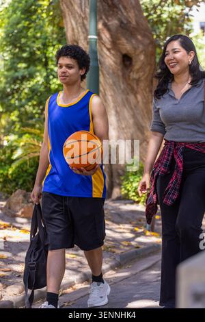 Divers amis marchant sur le chemin du parc portant du basket-ball orange et un sac de sport noir en maillot bleu Banque D'Images