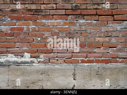 Gros plan horizontal d'un mur de briques rouges et de béton détérioré avec mortier écaillé fissuré, briques poreuses usées, ciment altéré Banque D'Images