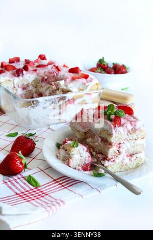 Tiramisu à la fraise italienne. Délicieux tiramisu à la fraise servi sur une assiette blanche, garni de menthe fraîche et de morceaux de fruits sur une nappe à carreaux Banque D'Images