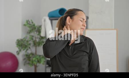 Jeune femme tenant la main au cou pour la douleur au cou après la formation de yoga, effectuant l'étirement du cou dans un studio de yoga ; récupération de la douleur. Banque D'Images