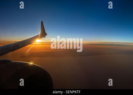 Une vue aérienne à couper le souffle capturée depuis la fenêtre passager d'un avion, montrant l'extrémité des ailes tandis qu'elle se silhouette sur un coucher de soleil éclatant et éclatant Banque D'Images
