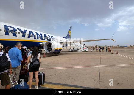 Passagers en attente d'embarquer sur un vol Ryanair à l'aéroport Marrakech-Menara, Maroc. Maroc, Marrakech - 12 août 2023 : un groupe de voyageurs avec leurs bagages attendant sur le tarmac pour embarquer à bord d'un avion Ryanair à l'aéroport RAK de Marrakech-Menara. Certains passagers grimpent déjà les escaliers de l'avion sous un ciel nuageux. Marrakech Maroc Copyright : xGennaroxLeonardix Banque D'Images