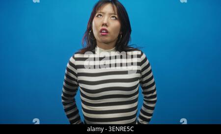Femme versant les lèvres avec inclinaison de la tête et les mains sur les hanches portant un pull rayé noir et blanc et boucles d'oreilles cerceau, studio ; gêne sassy. Banque D'Images
